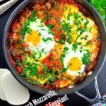 Vegetarian Passover Recipes: A Bird's eye view of a pan of Fresh Mozzarella, Mushroom and Eggplant Shakshuka, in a rich tomato sauce, with 2 eggs on top and generously sprinkled with chopped parsley. On the table surface there are 2 silver forks, a bunch of cilantro, 2 fresh tomatoes and 2 slices of fresh mozzarella.