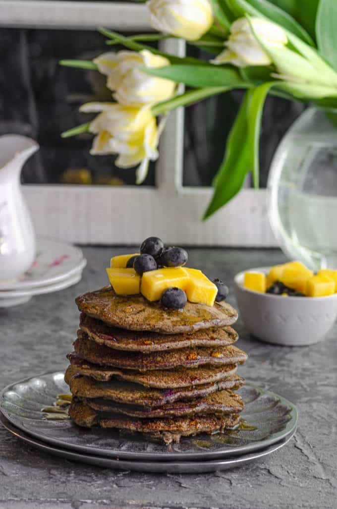 Side view of a stack of buckwheat pancakes topped with diced mangoes na blueberries