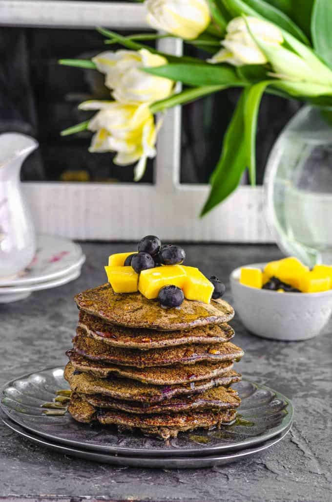 Side view of a stack of buckwheat pancakes topped with mangoes and blueberries