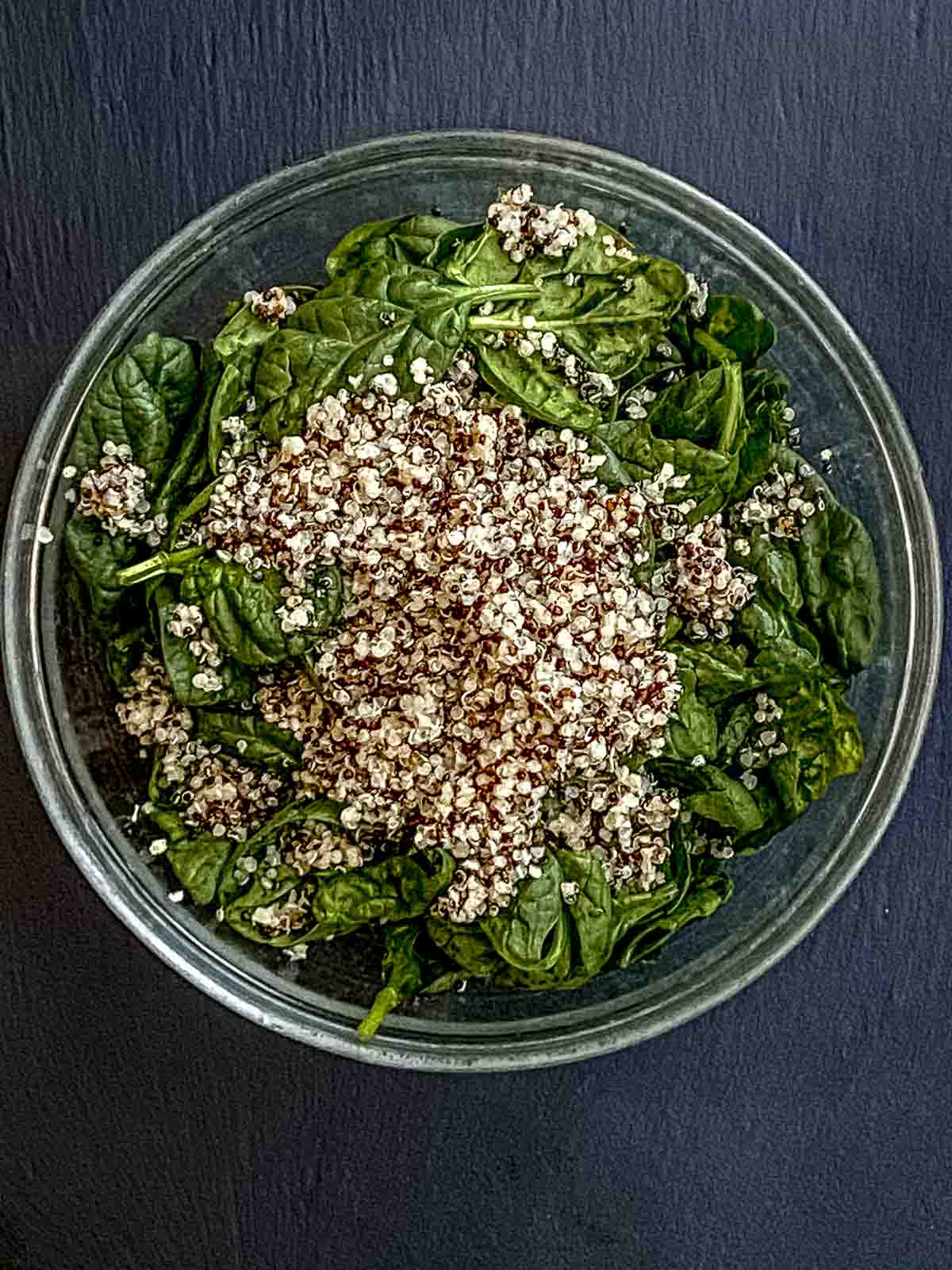 A glass bow with fresh baby spinach, and quinoa