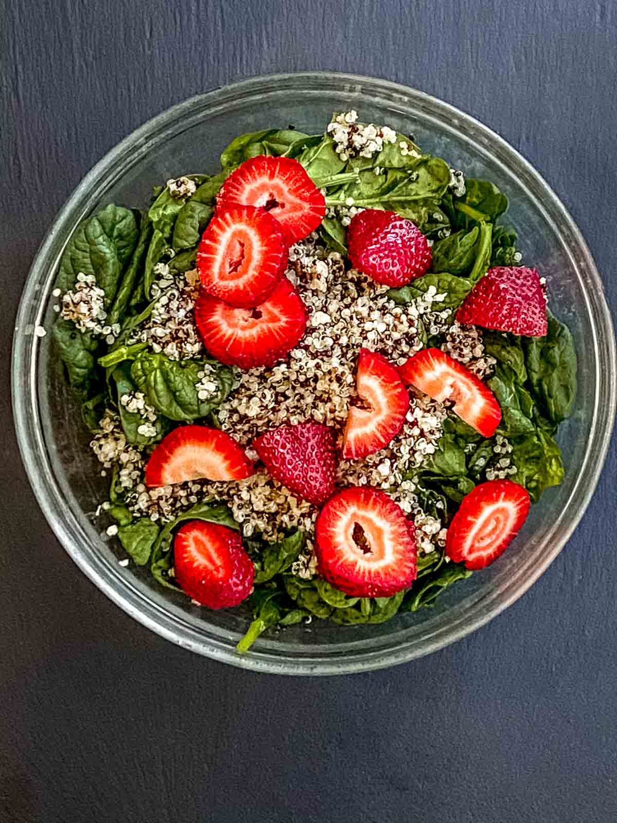A glass bow with fresh baby spinach, strawberries and quinoa