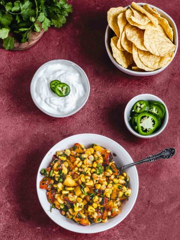 corn salsa next to a bowl of corn chips, sour cream and jalapenos