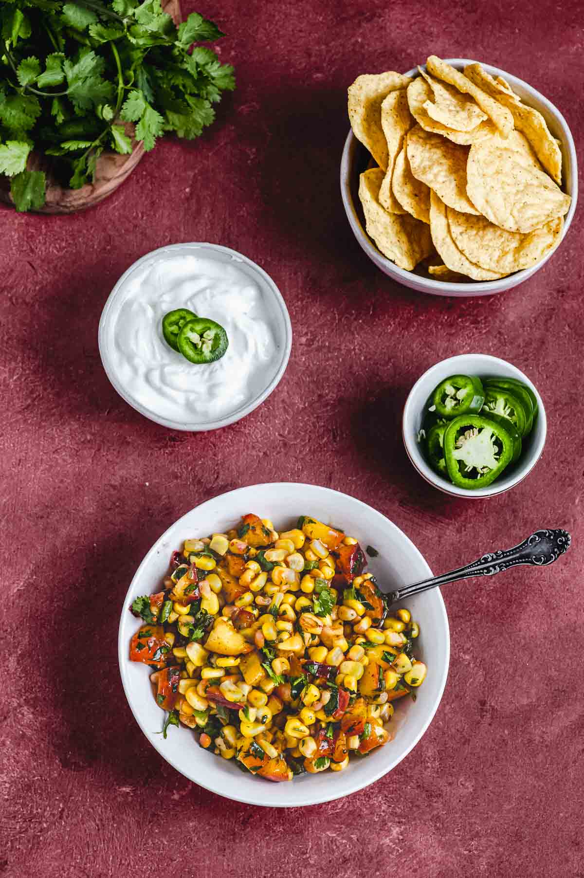 corn salsa next to a bowl of corn chips, sour cream and jalapenos
