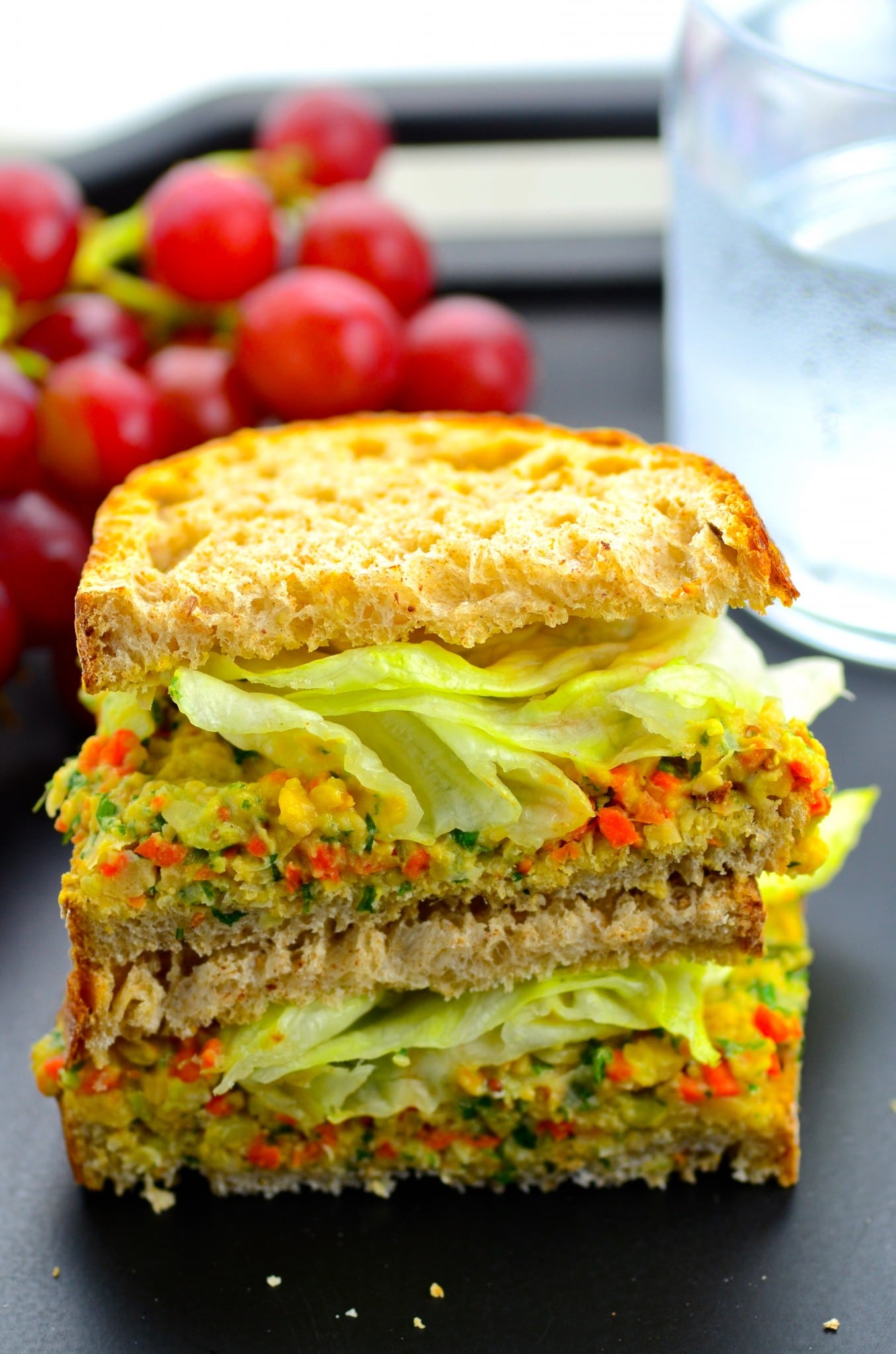 Side view of a smashed chickpea salad sandwich with grapes in the background