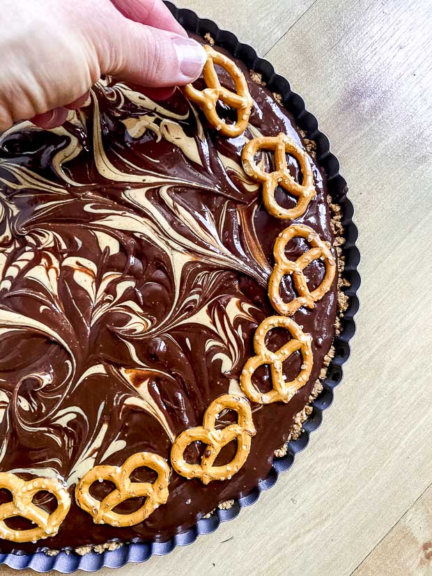 Placing pretzels around chocolate peanut butter tart.