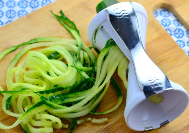 Spiralized zucchini noodles coming out of a manual vegetable spiralizer