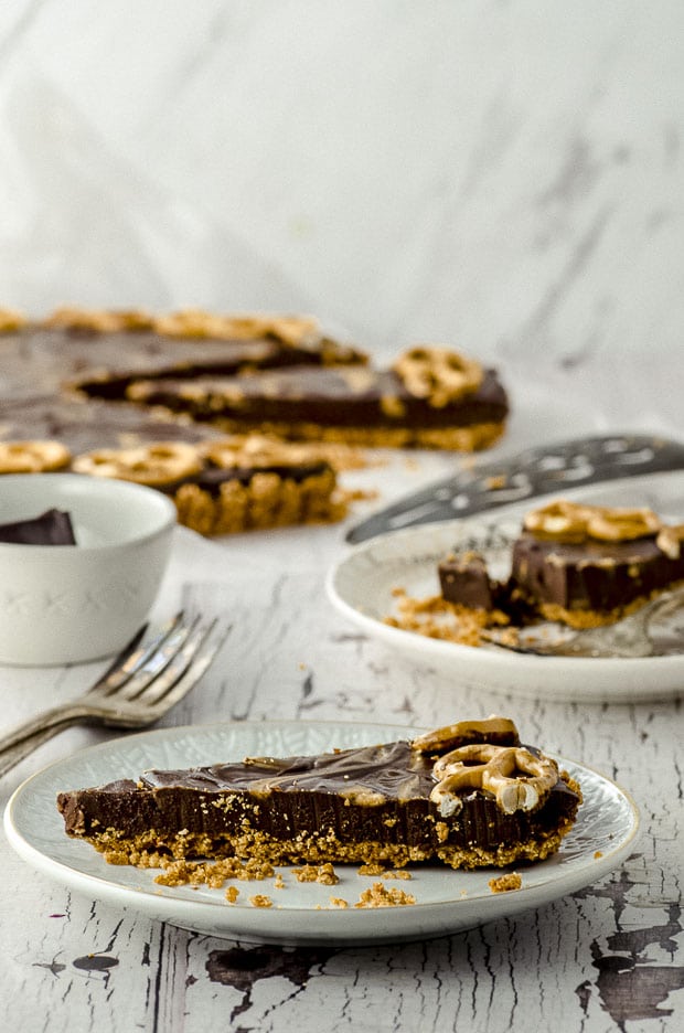 A close up view of a slice of chocolate peanut butter tart with  the whole tart in the background