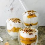 Three cups filled with pumpkin mousse with whipped topping , topped with ground dates and walnuts