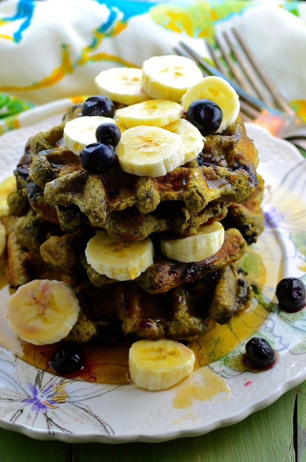 Side view of a pile of matcha waffles topped with fresh bananas and blueberries