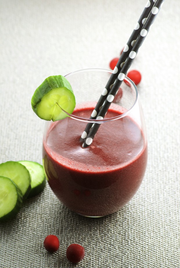 Close up view of a glass of a red smoothie with a slice of cucumber on the rim
