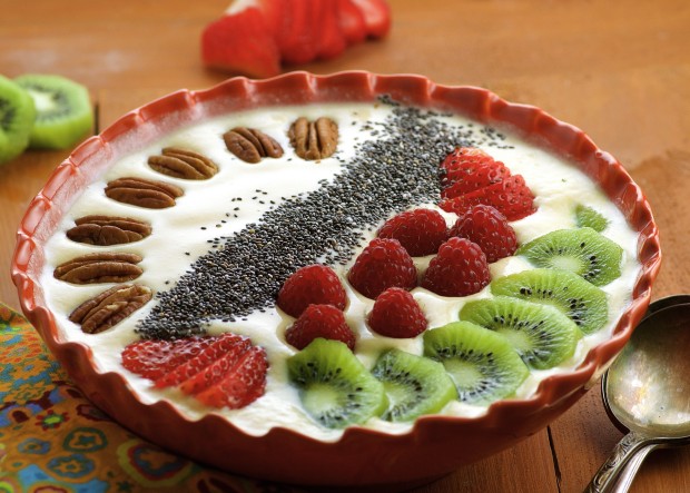 Side view of a smoothie bowl with sliced kiwis, fresh raspberries, strawberries, chia seeds and pecans.