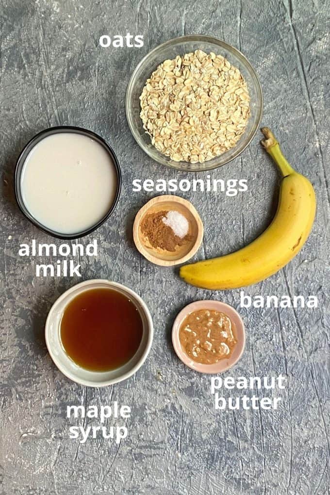 An overhead view of the ingredients to make peanut butter banana baked oatmeal; oats, almond milk, seasonings, banana, maple syrup, and peanut butter