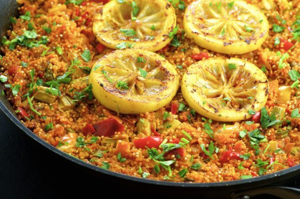 Close up of the Vegan Gluten Free Quinoa Paella garnished with four slices of roasted lemon in a paella pan