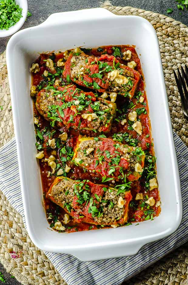  Vue à vol d'oiseau de bateaux de courgettes farcies au quinoa sur un plat de cuisson blanc.Une de nos recettes végétariennes pour la Pâque.