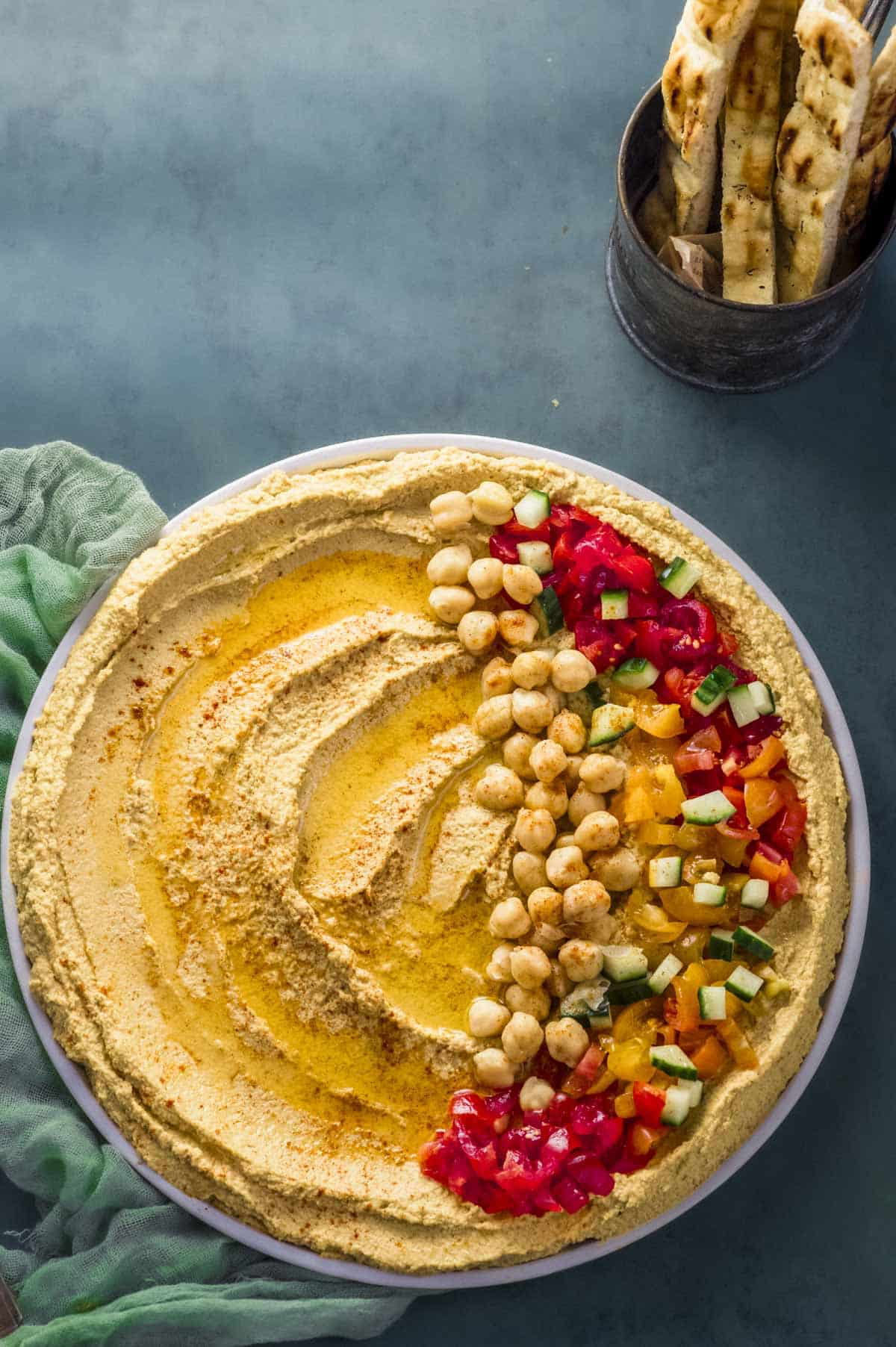 Overhead view of a round plate with roasted cauliflower hummus garnished with tomatoes cucumbers and chickpeas