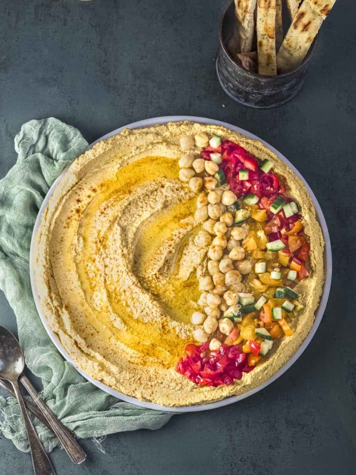Overhead view of a plate with cauliflower hummus topped with tomatoes, cucumbers and chickpeas