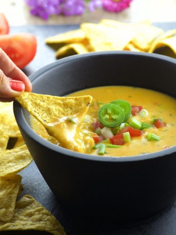 Dipping a corn chip in a black bowl filled with vegan queso dip