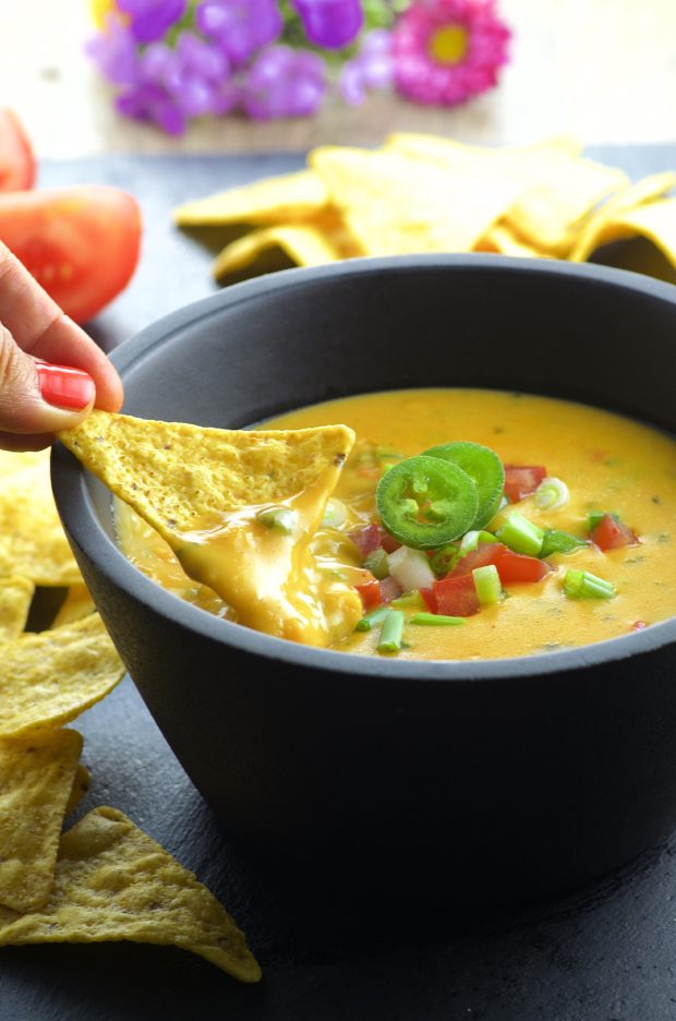 Scooping vegan queso dip with a corn chip
