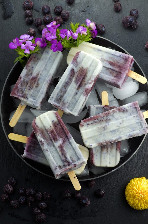 Birds eye view of the blueberries and cream popsicles in a metal bowl woth some purple flowers