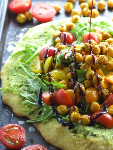Side view of a ricotta pizza topped with tomatoes and spiced chickpeas and drizzled with a tangy pomegranate reduction.