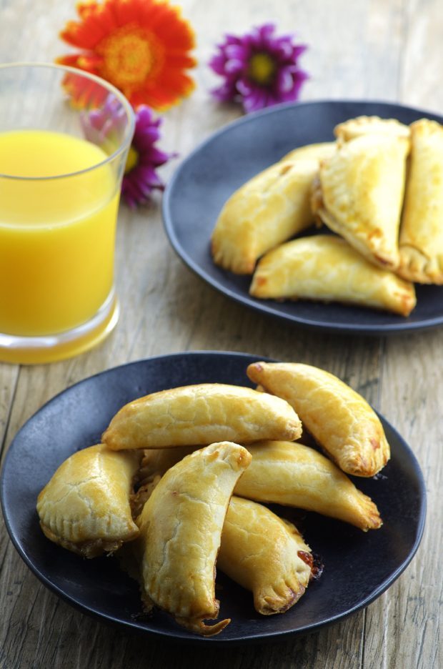two black plates filled with fig and cheese empanadas with a glass of orange juice in the background