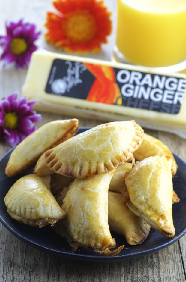 A black plate with a pile of fig and cheese empanadas with a blog of orange ginger cheese in the background