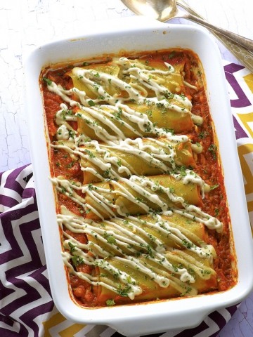 A white baking dish with high protein pumpkin cannelloni placed on tomato sauce