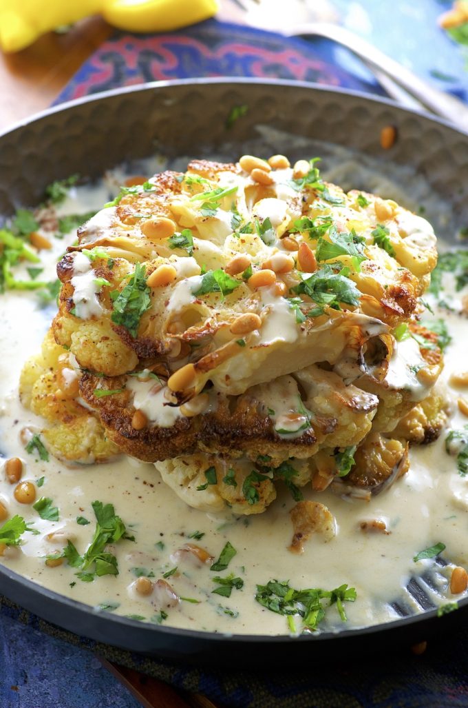 Side view of Roasted Cauliflower Steaks with Tahini and Pine Nuts on a black plate