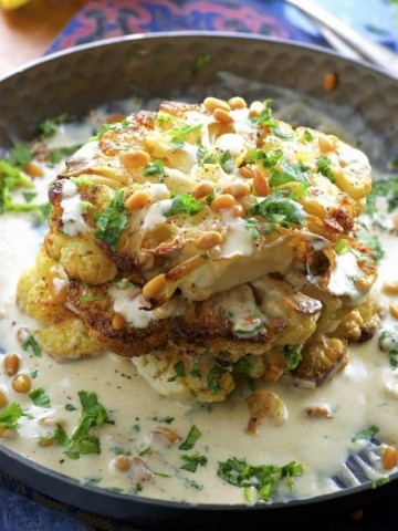 Side view of Roasted Cauliflower Steaks with Tahini and Pine Nuts on a black plate