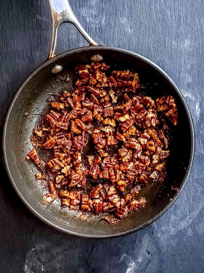 An overhead view of pecans on a skillet being coated
