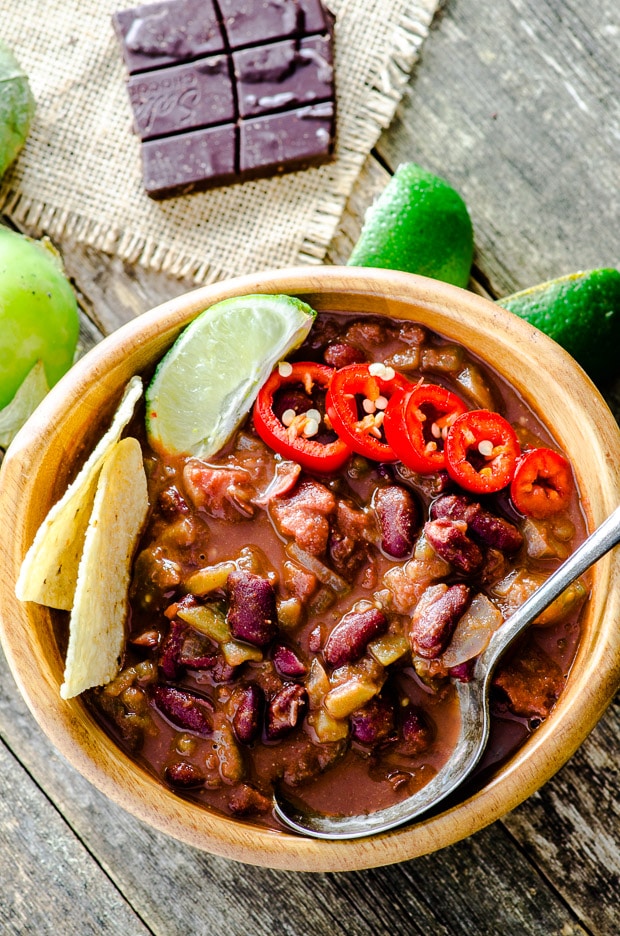 Birds eye view of a wood bowl filled with cayenne chocolate vegan chili topped with lime slices and hot pepper slices