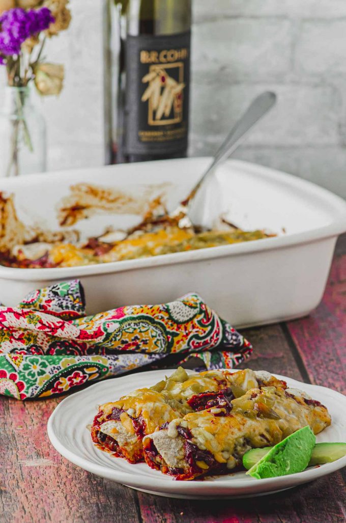 a plate with two vegetarian enchiladas with a baking dish and a bottle of wine on the background