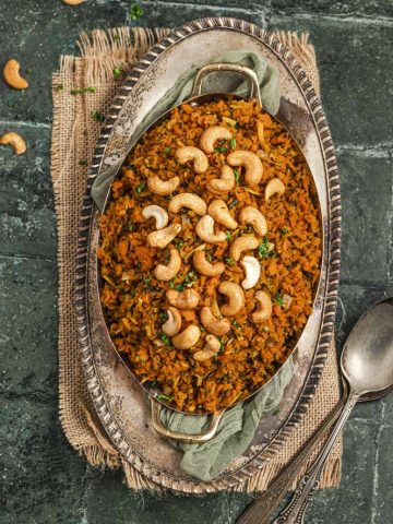 Close up view of an oval serving dish with passover carrot rice topped with cashews.