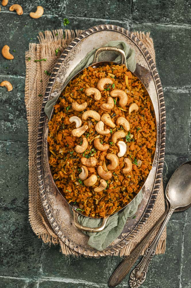Close up view of an oval serving dish with passover carrot rice  topped with cashews.