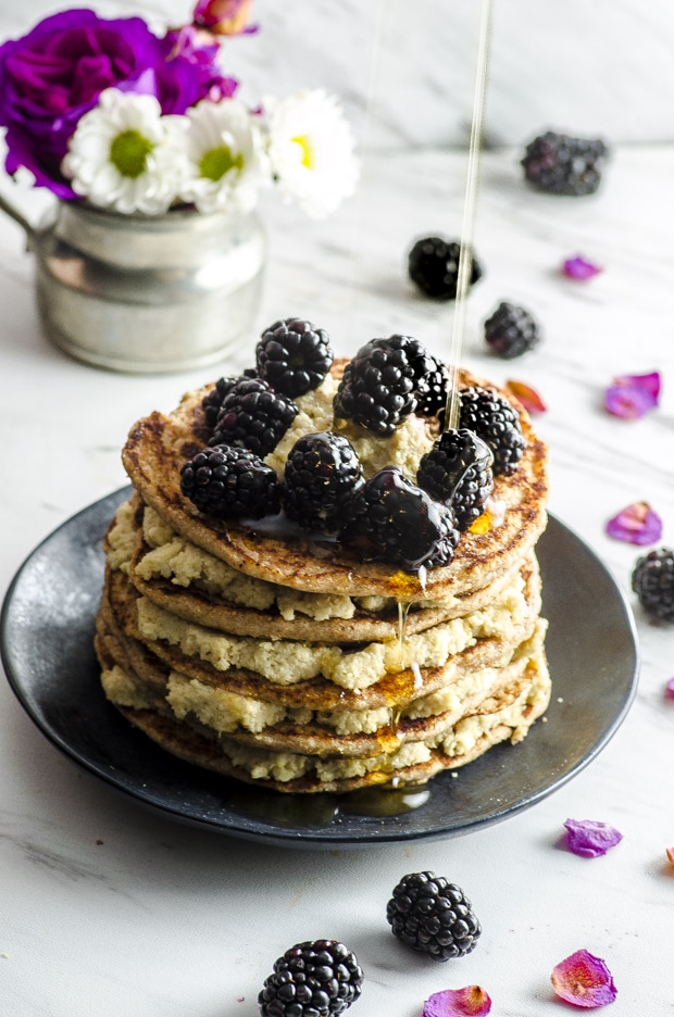 A stack of whole wheat pancakes layered with lemon cashew ricotta topped with blackberries, with a drizzle of maple syrup