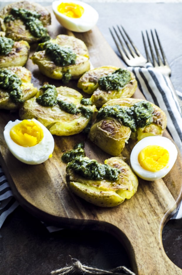 Smashed Potatoes with Chimichurri Sauce on a wooden cutting board with a hard boiled egg sliced in half