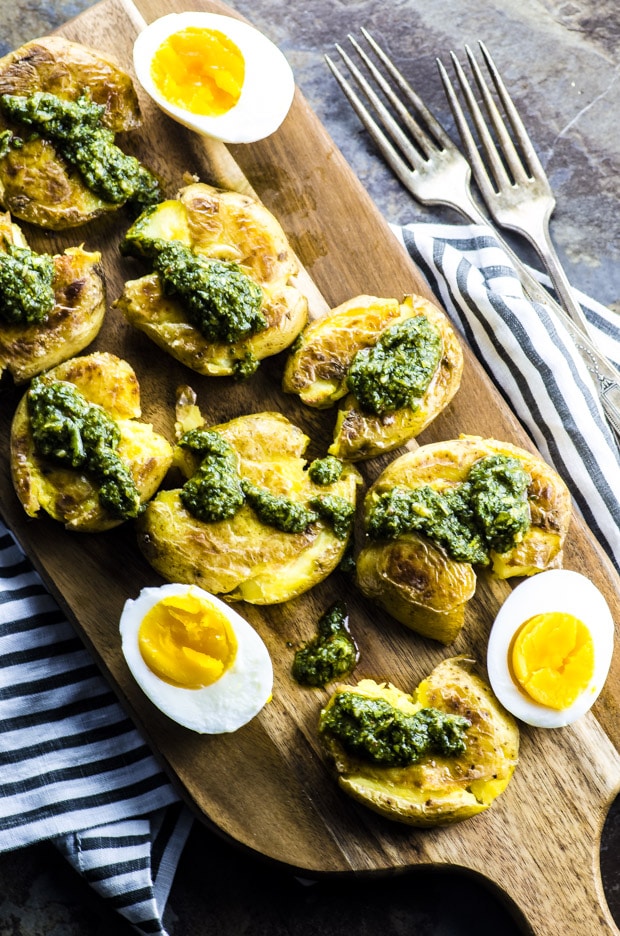 Birds eye view of Smashed Potatoes with Chimichurri Sauce on a wooden cutting board with a hard boiled egg sliced