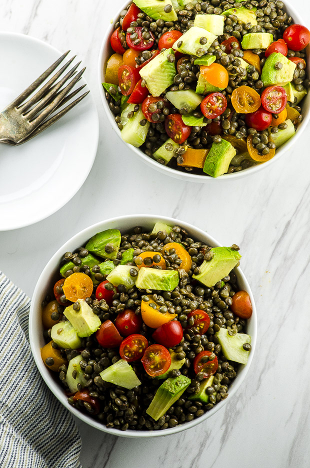 Birds eye view of two bowls of avocado tomato lentil salad on a white surface