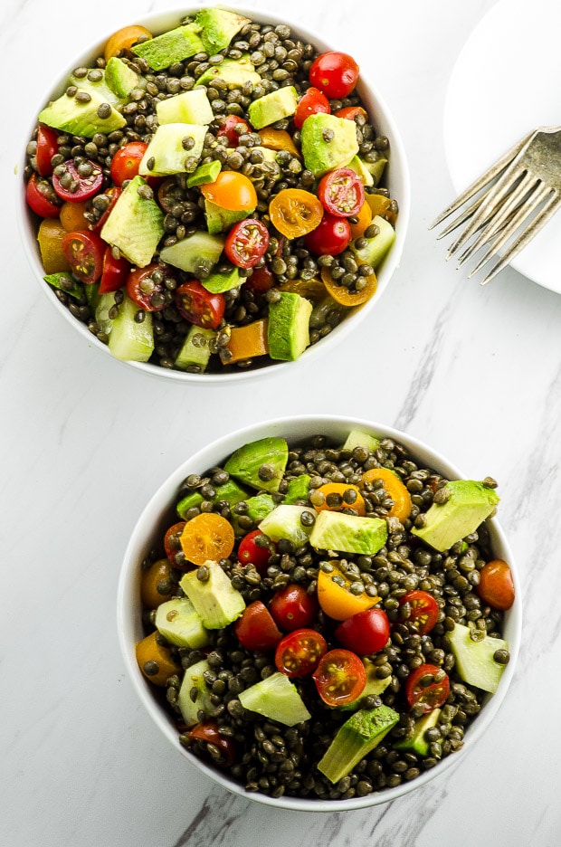 Birds eye view of two bowls of avocado tomato lentil salad on a white surface