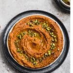 Roasted red pepper hummus on a plate garnishes with pistachios