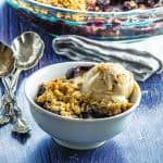 Side view of a bowl filled with blueberry crumble and topped with vanilla ice cream