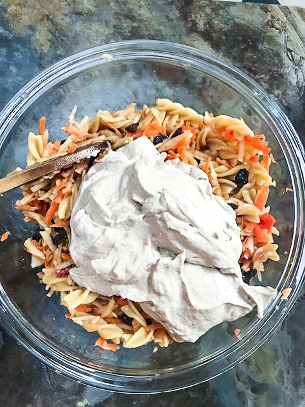 Glass bowl with chickpea fusilli, shredded apples, carrots and raisins and a big dollop of creamed tofu and cream cheese 