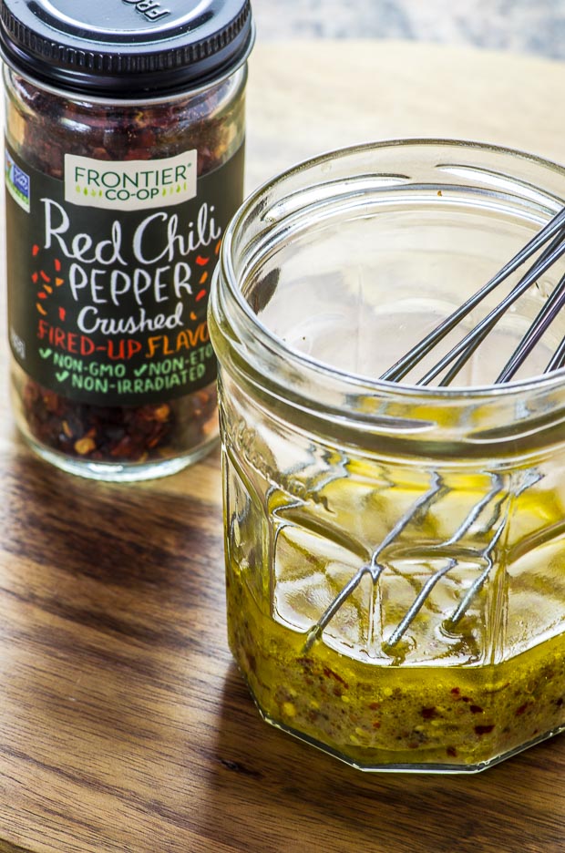 Glass jar with red chili pepper dressing with a whisk, and a small jar of Frontier bran crushed red chili pepper