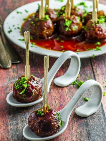 Vegetarian Sweet potato meatballs on two white spoons, covered in BBQ sauce and sprinkled with parsley.