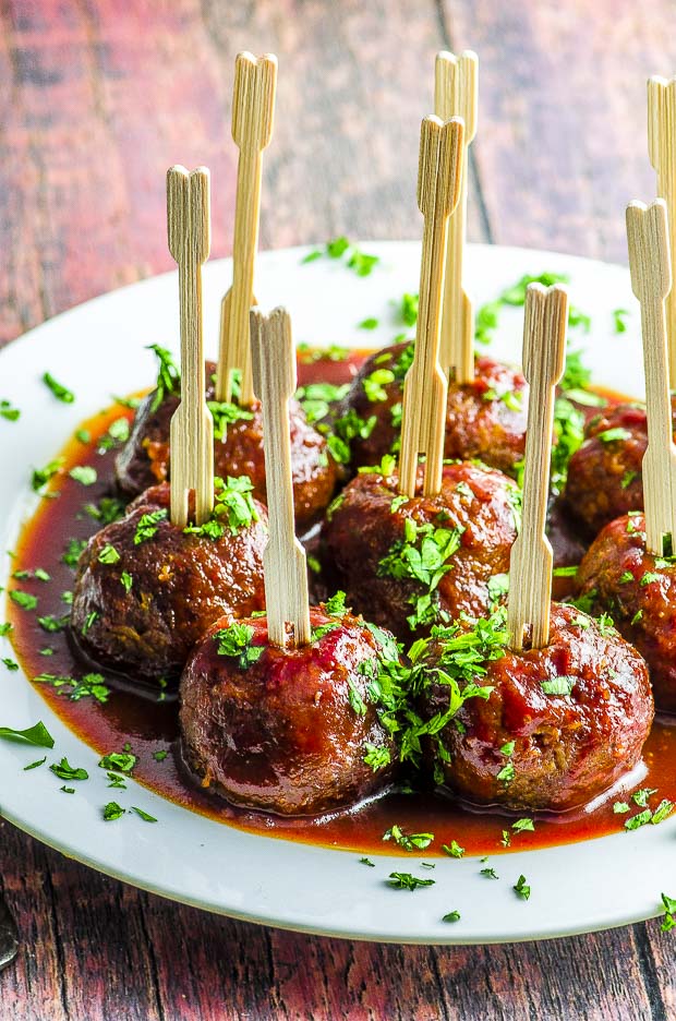 Vegetarian Sweet potato meatballs on a white plate, covered in BBQ sauce and sprinkled with parsley. Each meatball had a cocktail toothpick in it