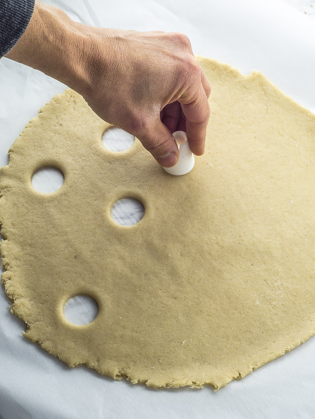 Rolled out pie dough on a piece of white parchment paper, with small circles being cut out with a piping bag tip