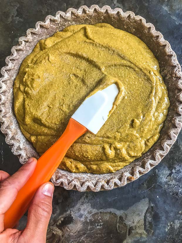 Birds eye view of the unbaked pie shell, with vegan pumpkin filling being spread with a spatula