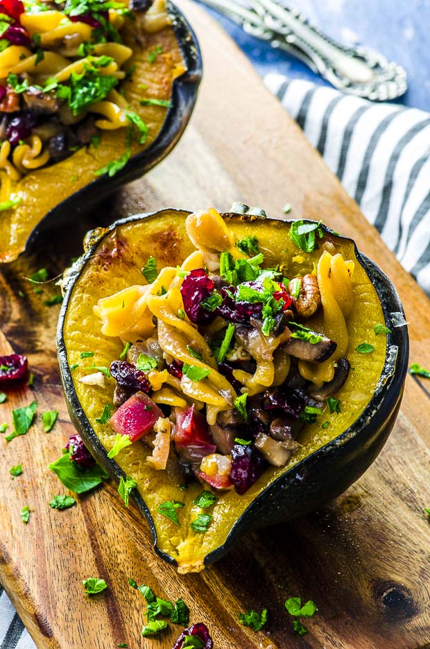 Half a baked stuffed acorn squash on a wooden board with some chopped parsley scattered around and the other half of the squash in the background
