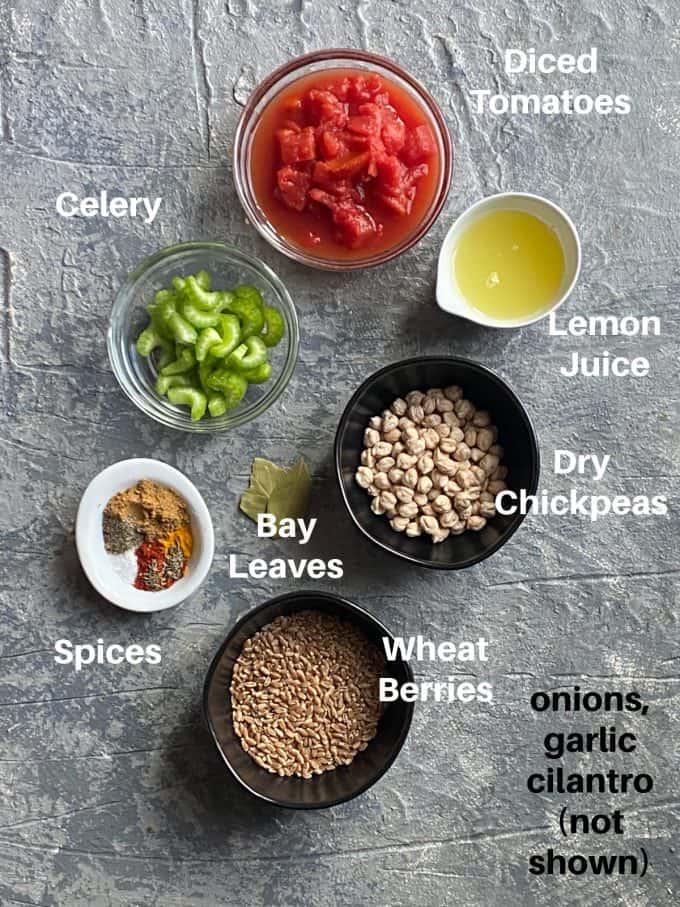 overhead shot of the ingredients used for the chickpea soup. dried chickpeas, wheat berries, diced tomatoes, celery, onion, garlic, spices . lemon juice and cilantro