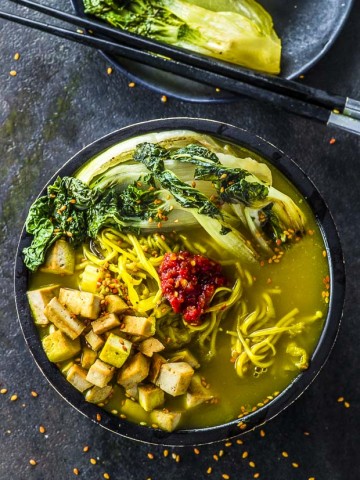 Birds eye view of a black bowl with Immune Booster Vegan Ramen. The vegan ramen is topped with seared baby boy choy, ramen noodles, spicy garlic sauce and saute tofu square.